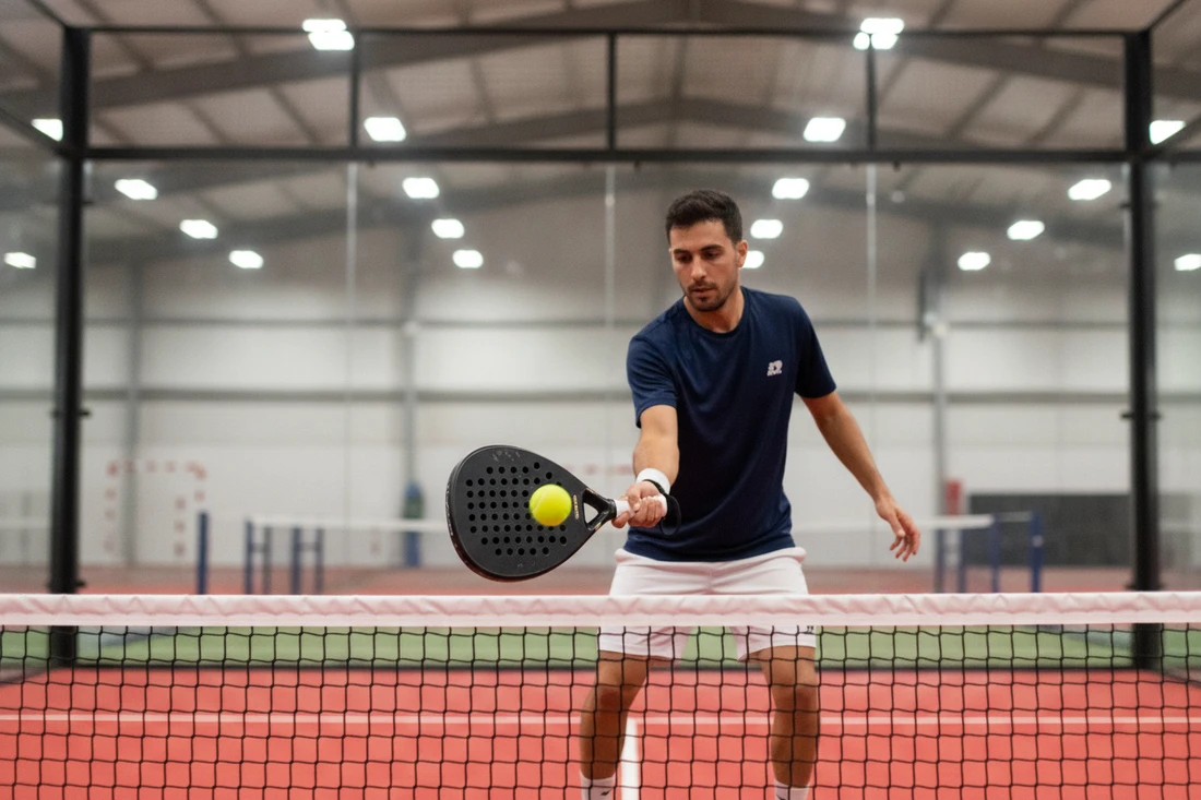 Gros plan du geste d'amortie au padel, main relâchée, terrain indoor rouge
