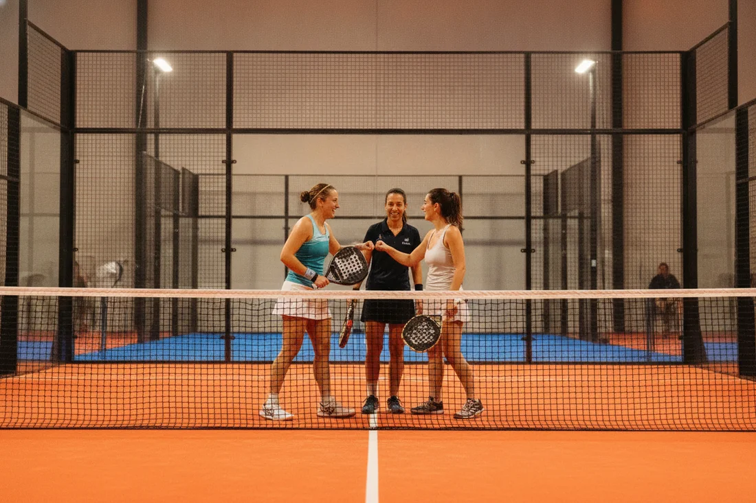 Quatre joueurs de padel souriants partageant un moment convivial, terrain indoor orange