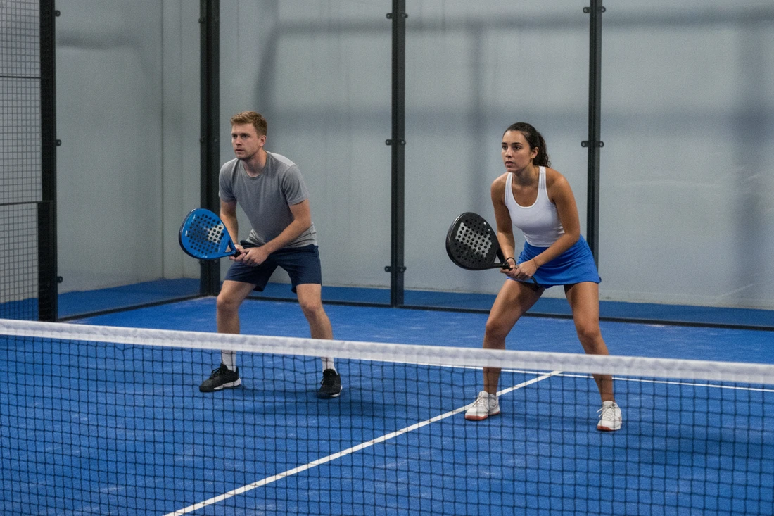 Paire de padel répartie côté droit et gauche en position, terrain indoor bleu