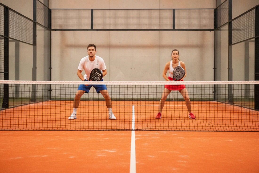 Paire de padel répartie côté droit et côté gauche sur un terrain indoor au sol orange