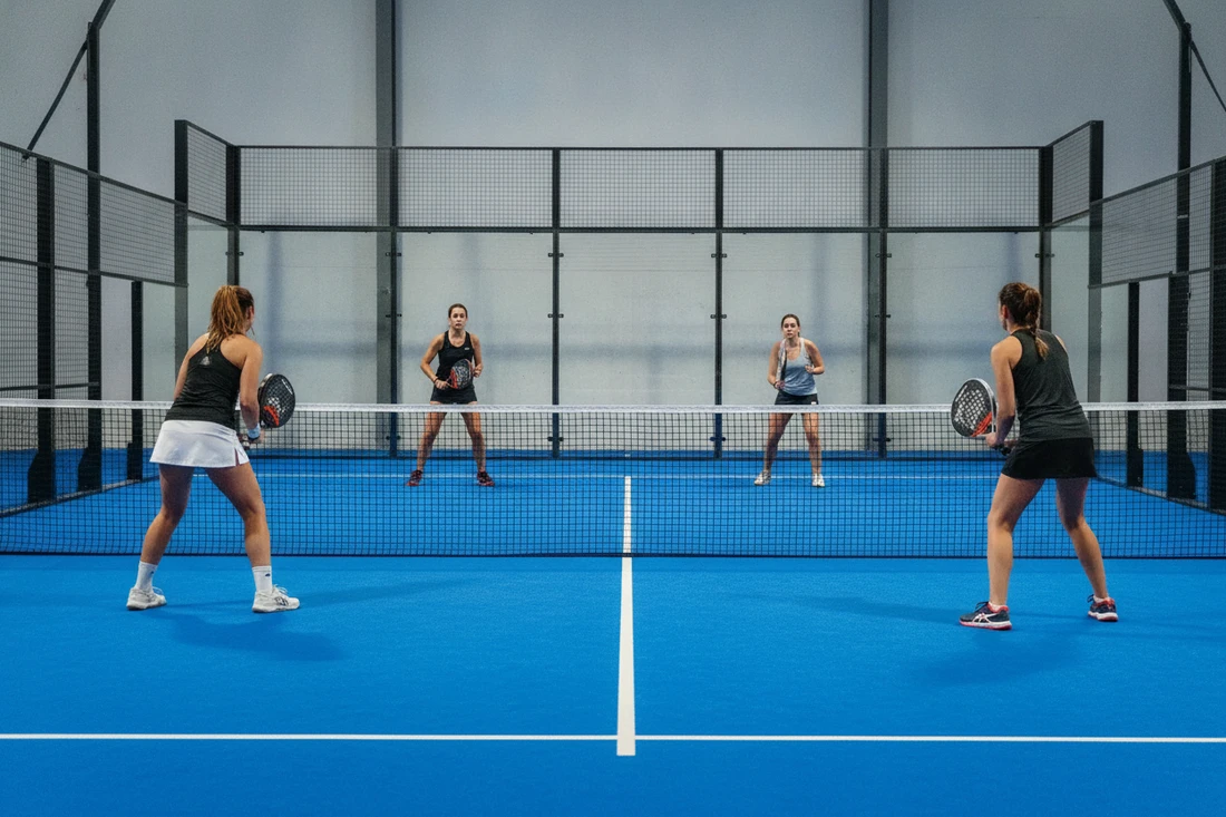 Joueurs de padel à l'entraînement simulant des points sous pression, terrain indoor bleu
