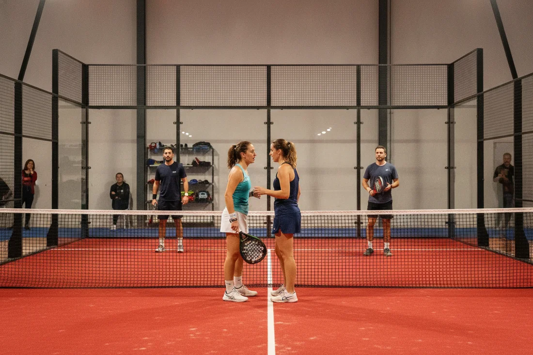 Paire de padel échangeant une consigne avant un point décisif, terrain indoor rouge