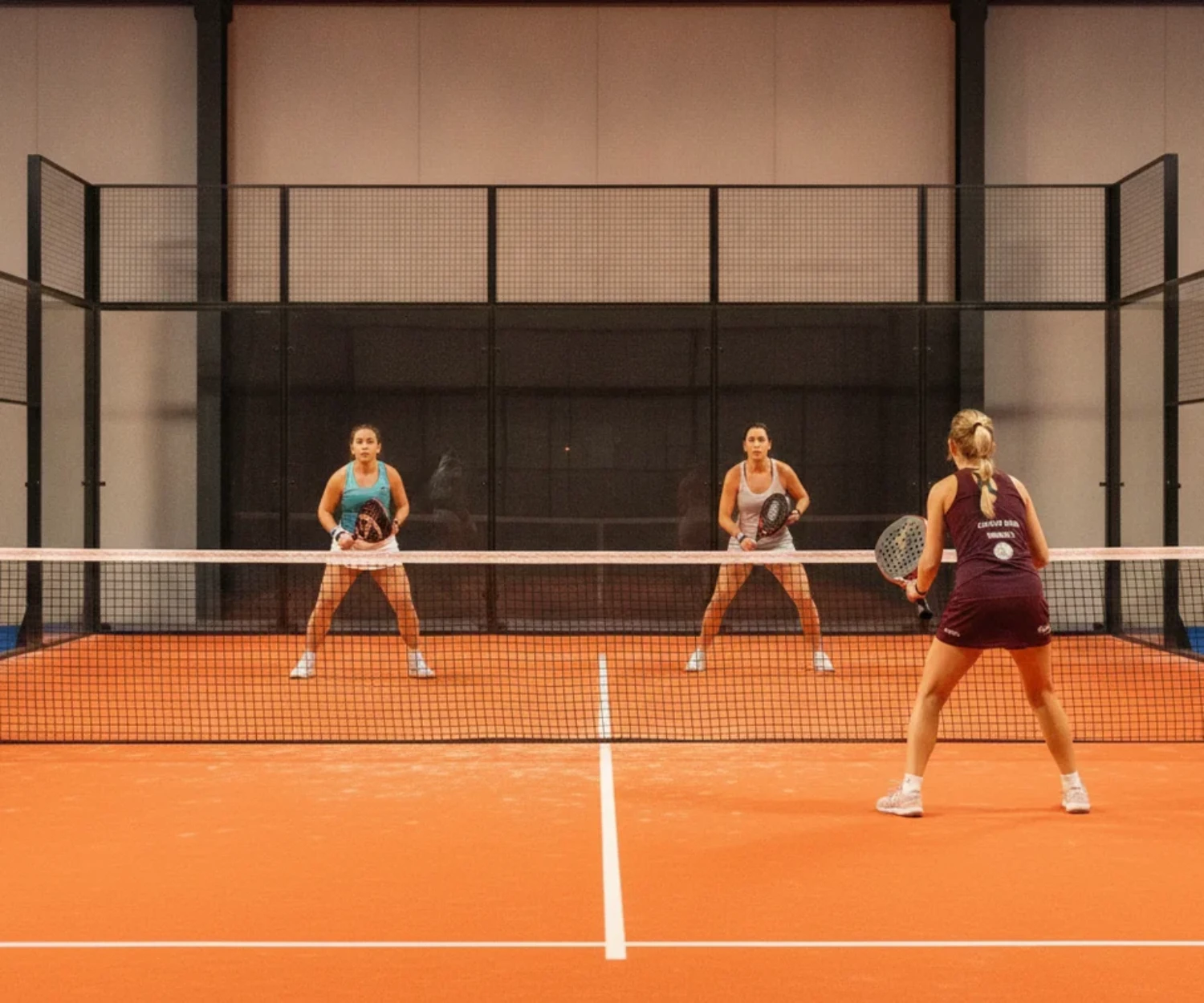 Match de padel en double à un moment clé, joueurs concentrés, terrain indoor orange