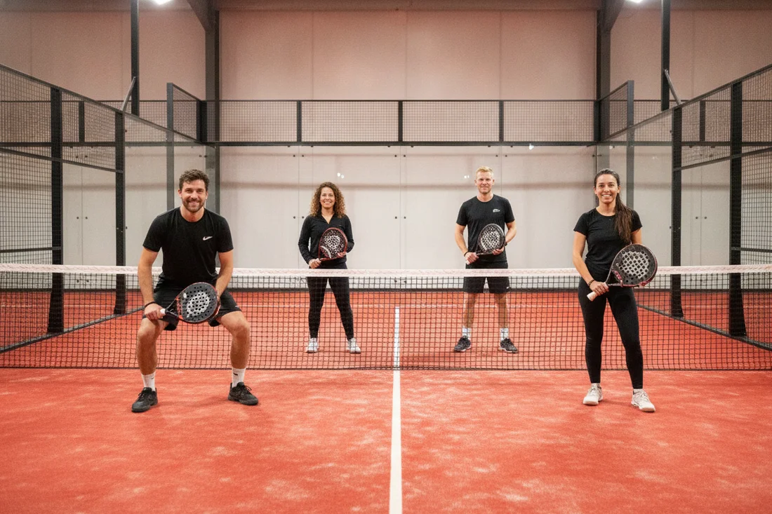 Partie de padel conviviale à quatre en indoor, sol rouge