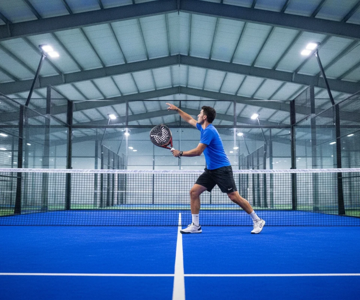 Joueur de padel en action face au filet sur un court indoor couvert au sol bleu