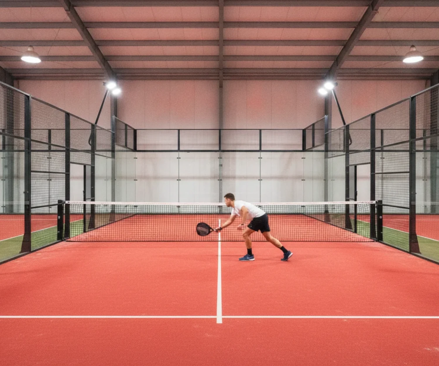 Joueur de padel en plein mouvement sur un vrai terrain clos avec portes d'entrée, terrain indoor rouge