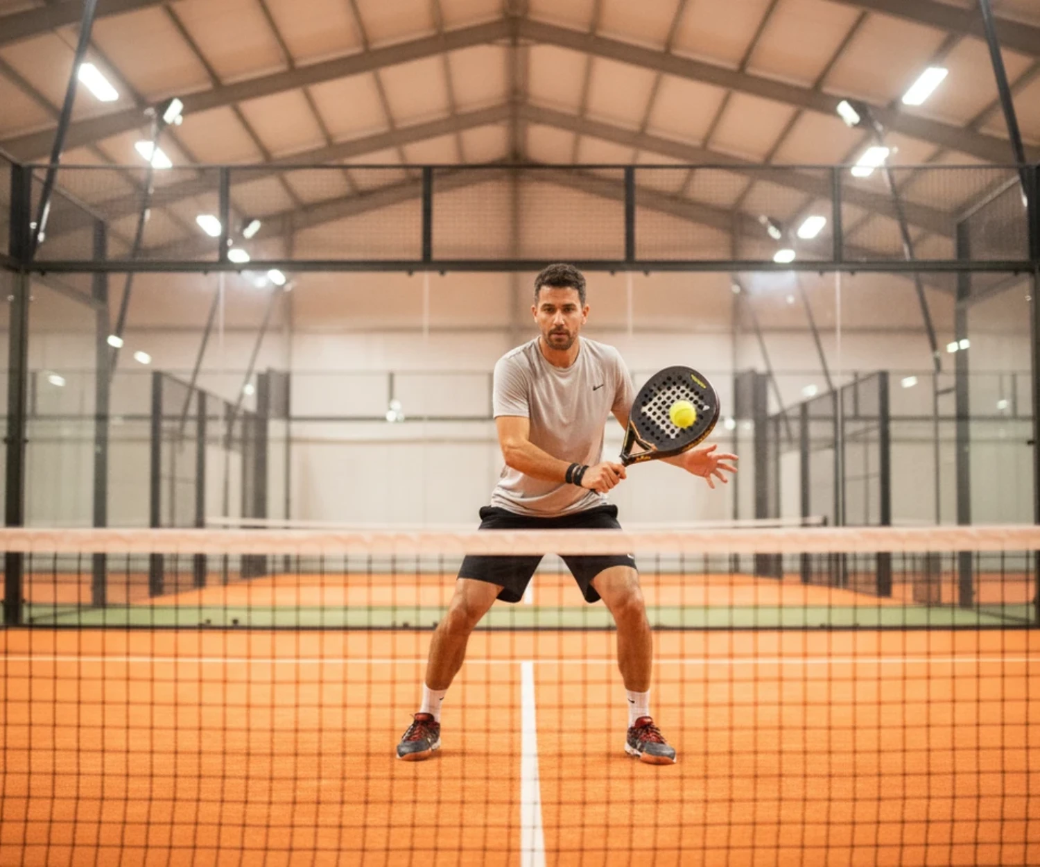 Joueur de padel à la volée au filet, progression, terrain indoor orange