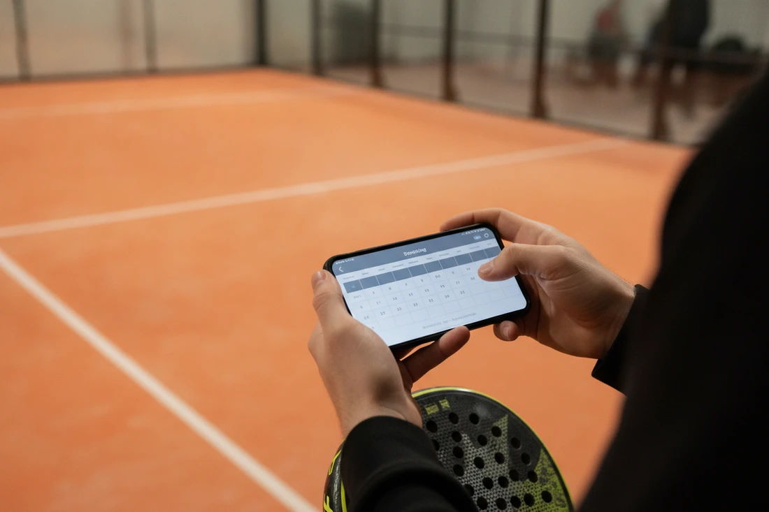Joueur réservant un terrain de padel sur une application mobile dans un club indoor au sol orange