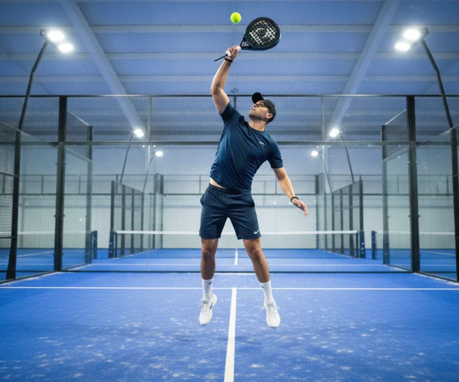 Joueur de padel exécutant un smash sur un court indoor bleu