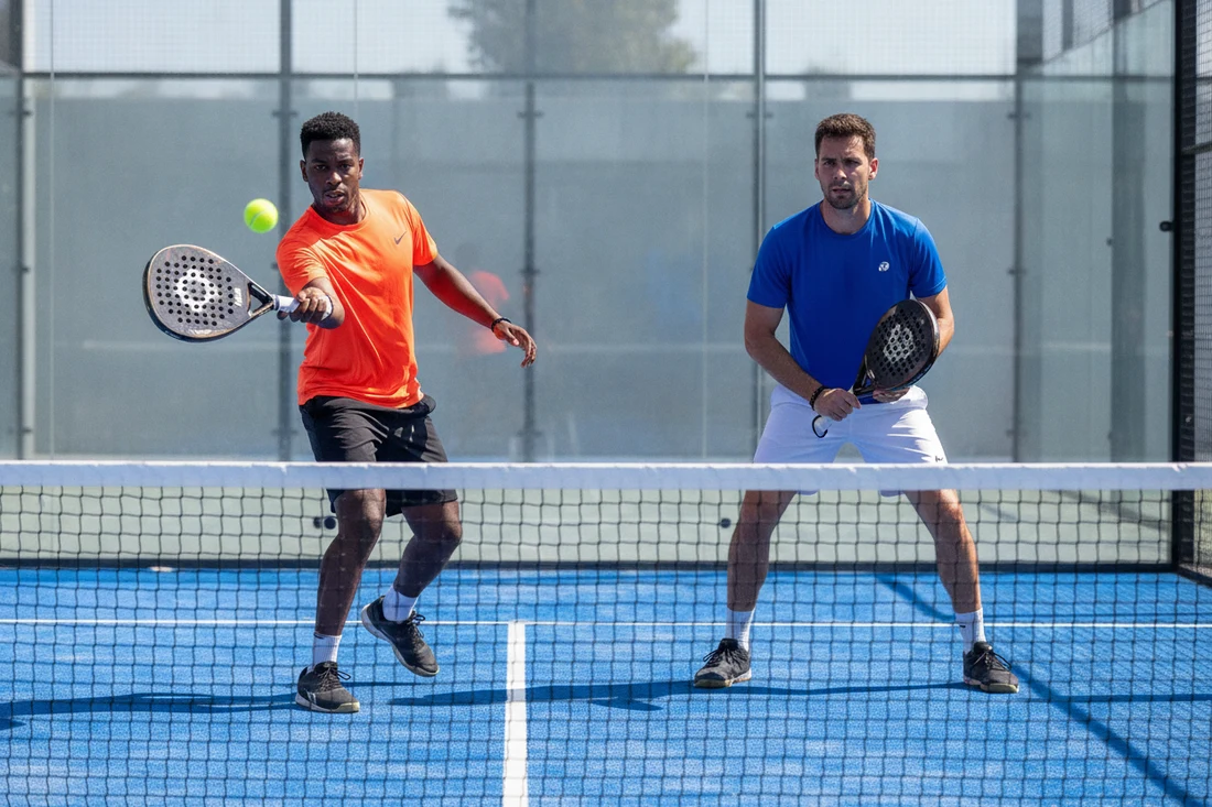Joueur de padel jouant la volee, son partenaire attentif raquette au centre