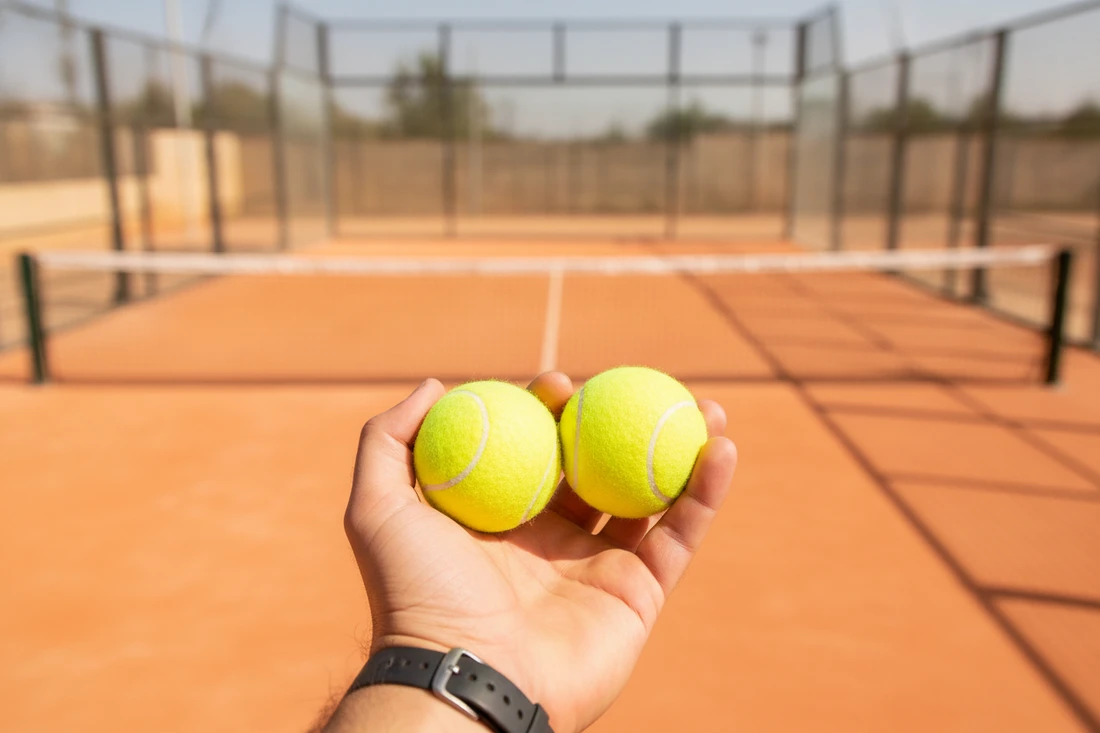 Main comparant l'usure de deux balles de padel au bord du court