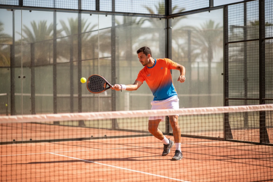 Joueur de padel frappant un coup droit puissant sur un court terracotta, raquette pleine en main