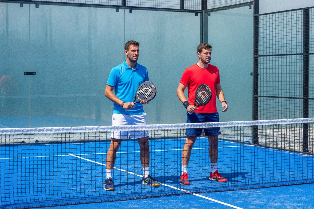 Paire de joueurs de padel en position d'attente au filet sur un court bleu