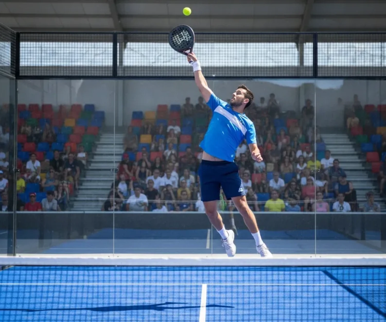 Joueur de padel exécutant un smash lors d'un tournoi Premier Padel dans une arène