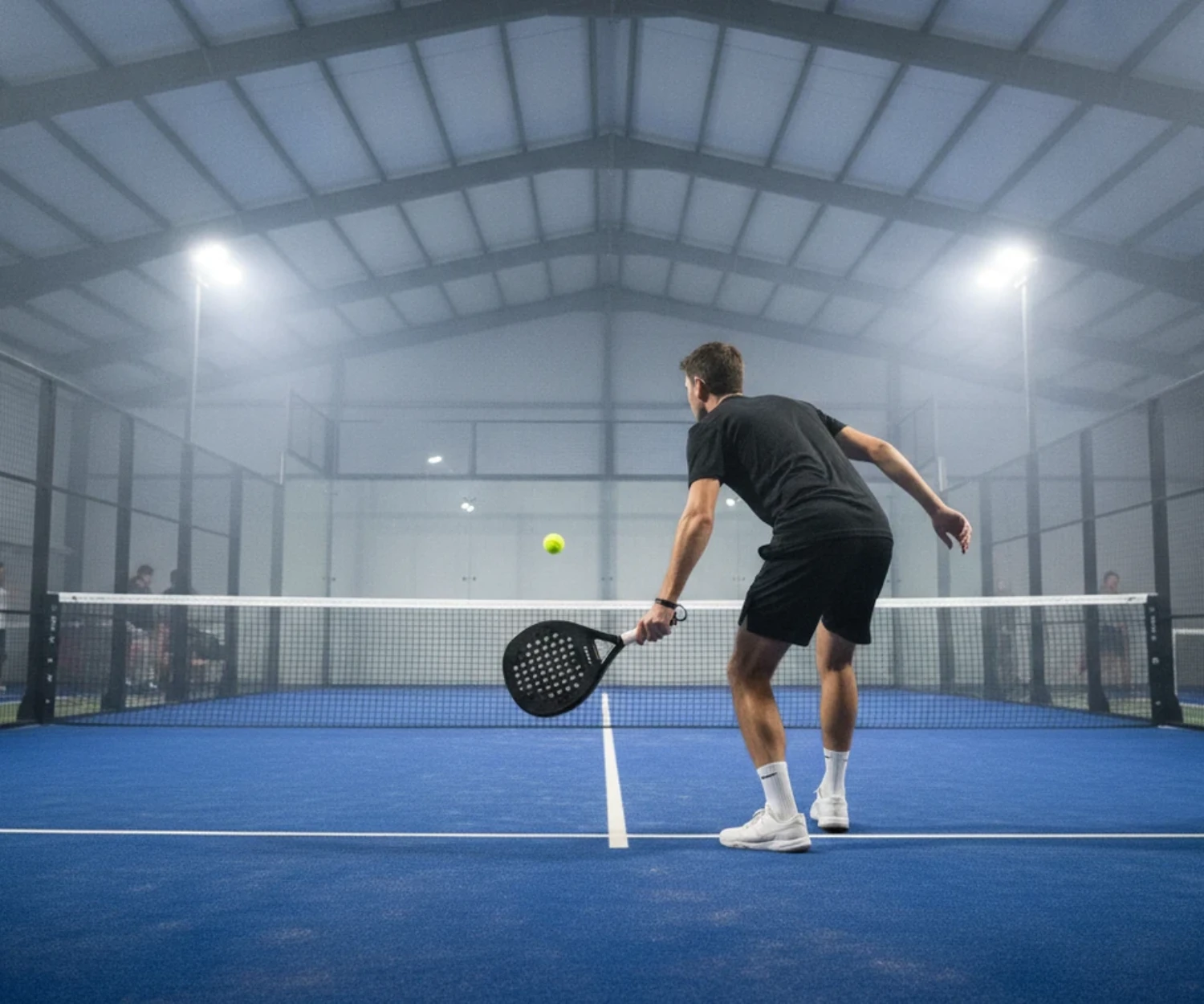 Joueur de padel au service a la cuillere sur un court indoor bleu