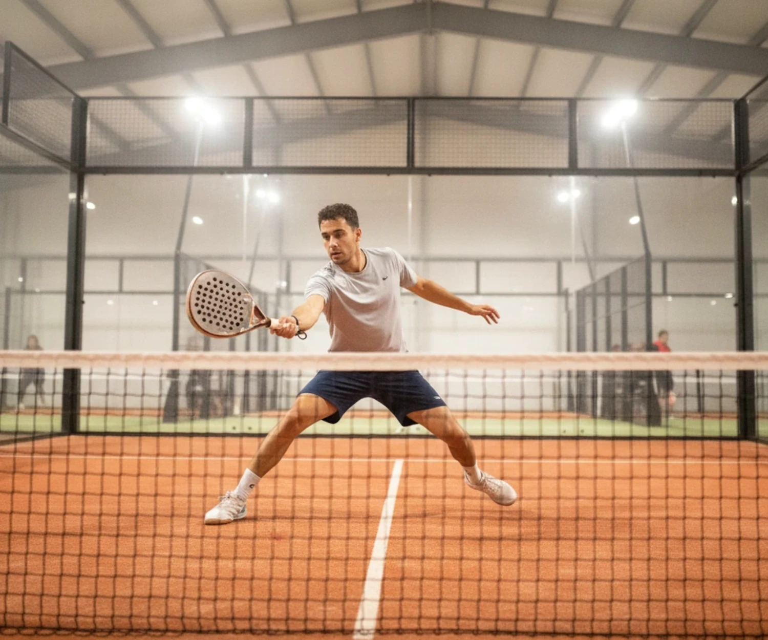 Joueur de padel en volée basse sur une piste indoor au sol orange, padel à Angers