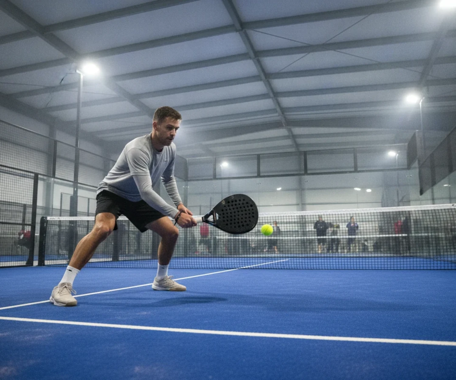 Joueur de padel frappant une balle basse sur une piste indoor bleue, padel à Brest