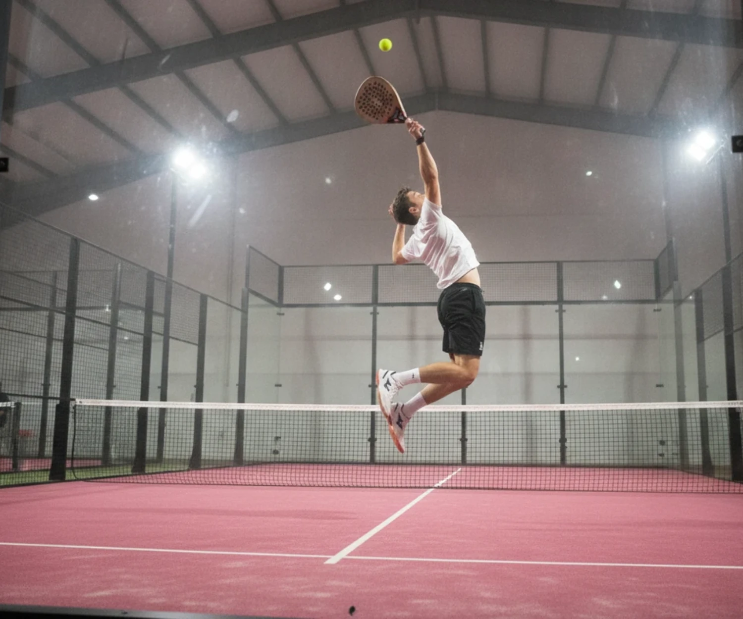 Joueur de padel au smash en suspension sur une piste indoor au sol rose, championnat de France de padel