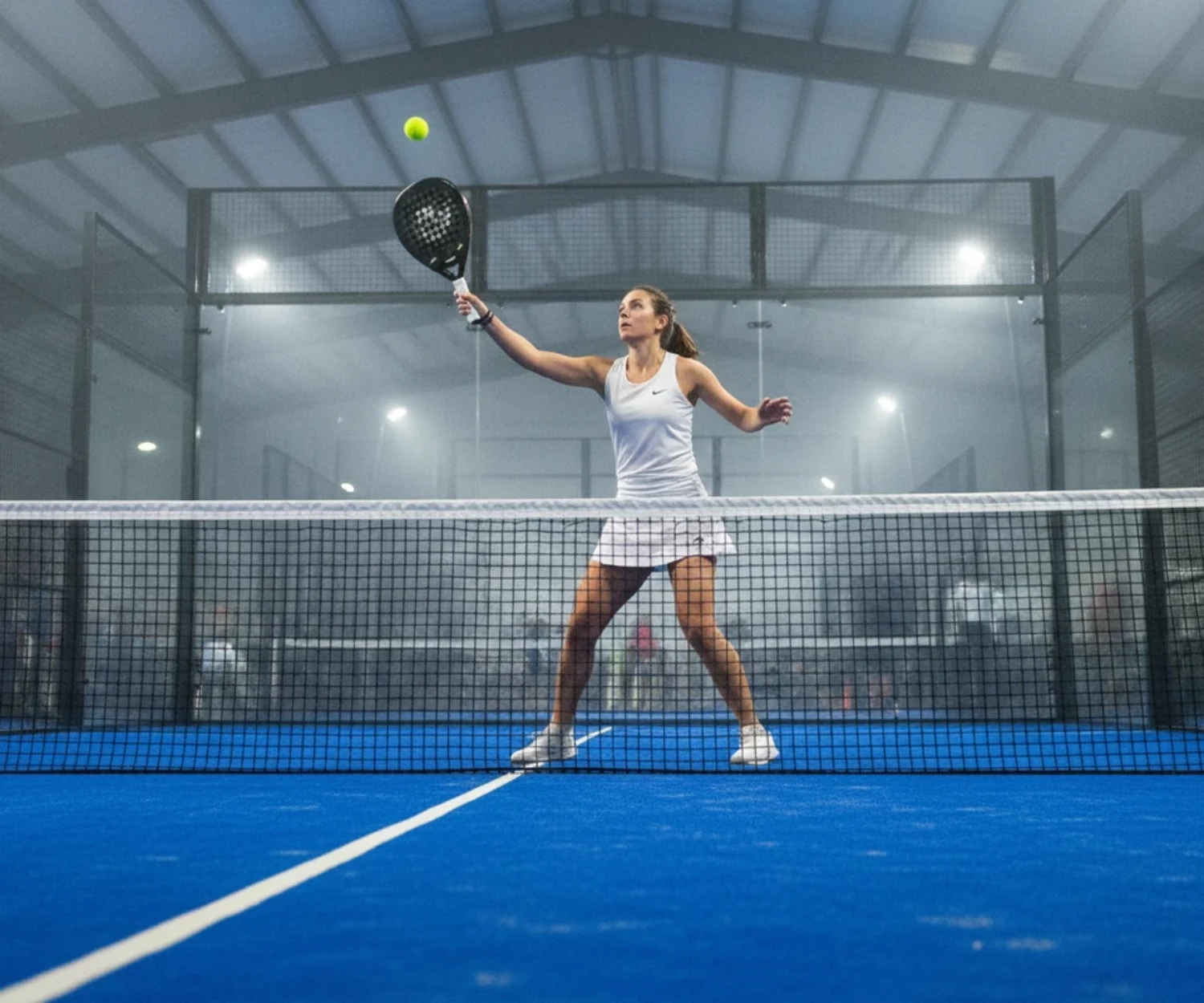 Joueuse de padel frappant une bandeja sur une piste indoor au sol bleu, padel femme en France