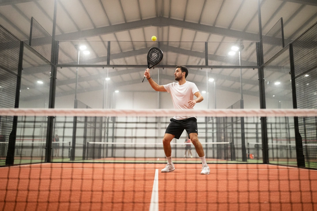 Joueur frappant une bandeja sur une piste de padel indoor au sol terre battue