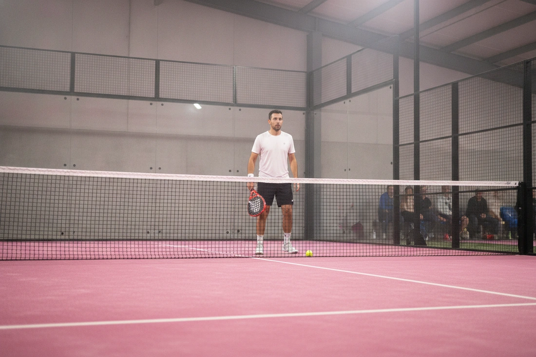 Joueur en position d'attente près de la vitre sur une piste de padel indoor rose