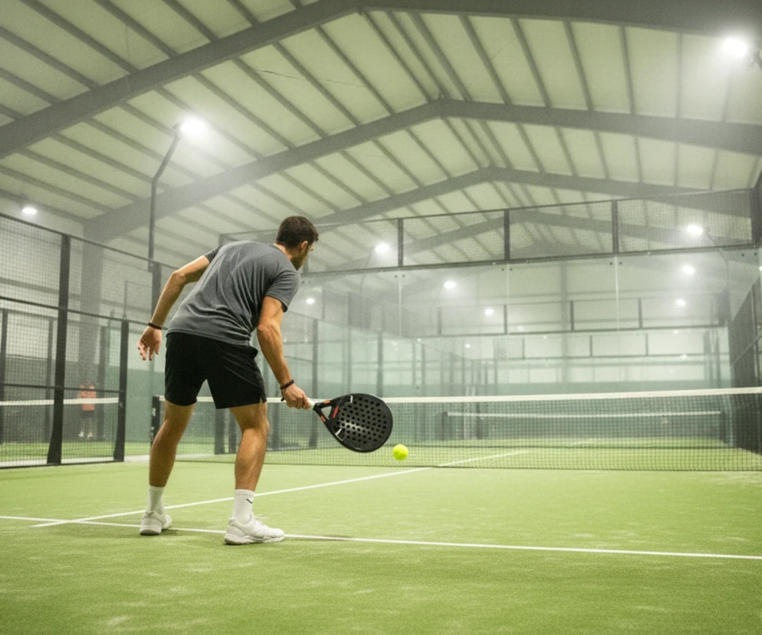 Joueur de padel au service sur une piste indoor au sol vert, padel à Nantes