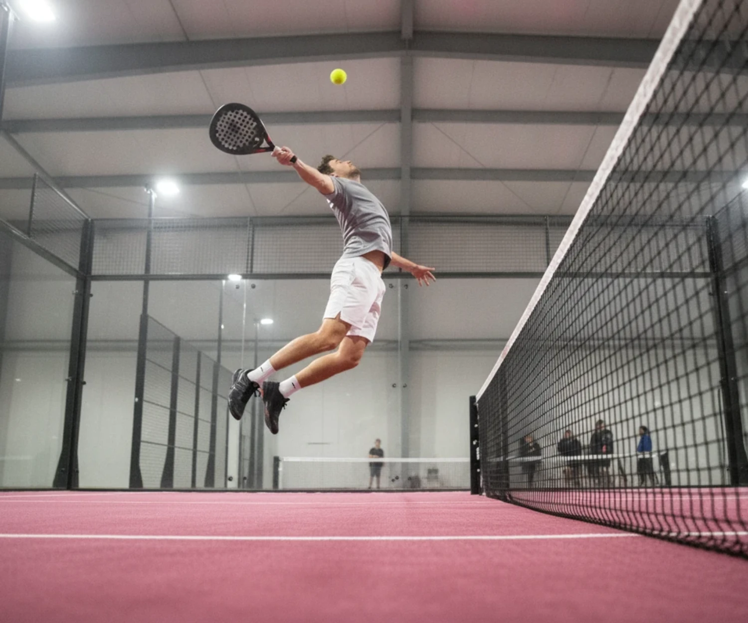 Joueur de padel au smash en suspension sur une piste couverte au sol rose, padel à Saint-Malo