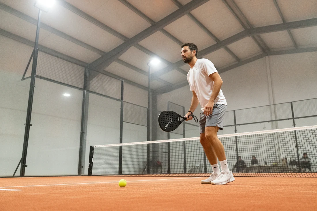 Joueur en attente sur une piste de padel indoor au sol orange, comme dans les clubs de padel à Vannes