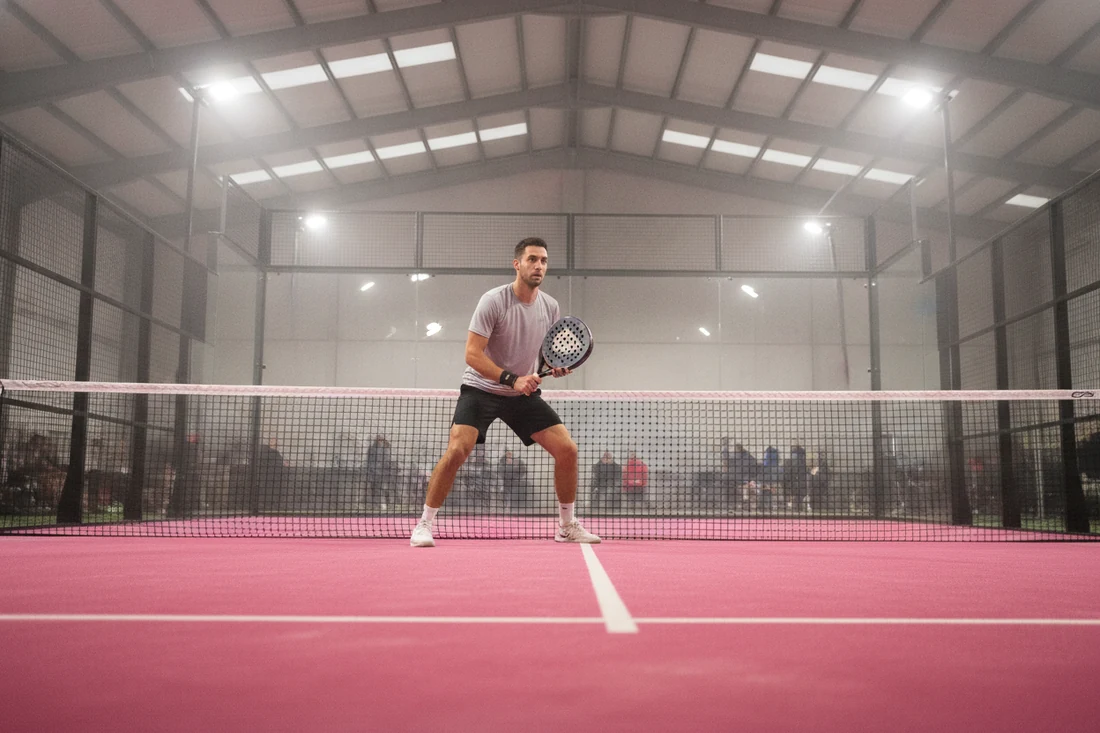 Joueur de padel en position d'attente, raquette tenue à deux mains, sur une piste rose couverte