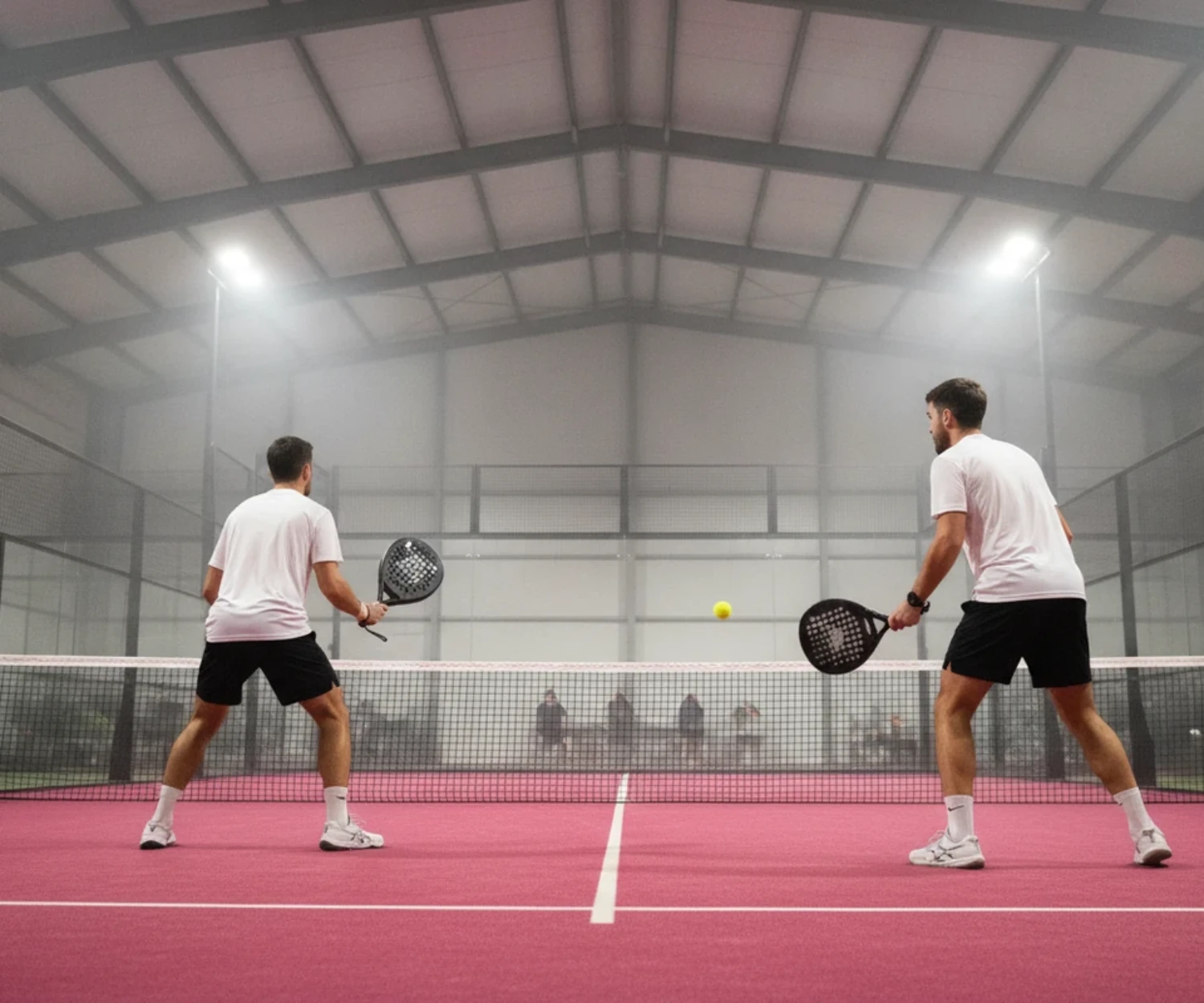 Deux partenaires de padel en position sur un court indoor rose, balle en jeu