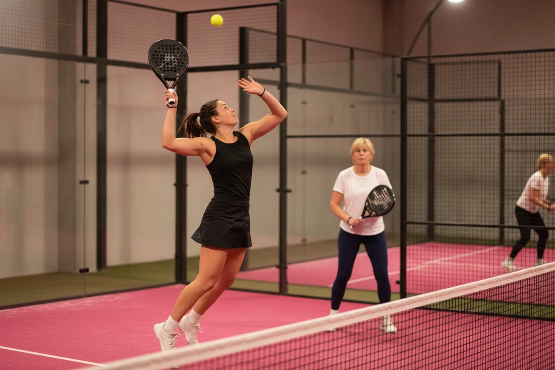 Une joueuse de padel smashe au filet sur une piste rose, sa partenaire en attente derrière elle