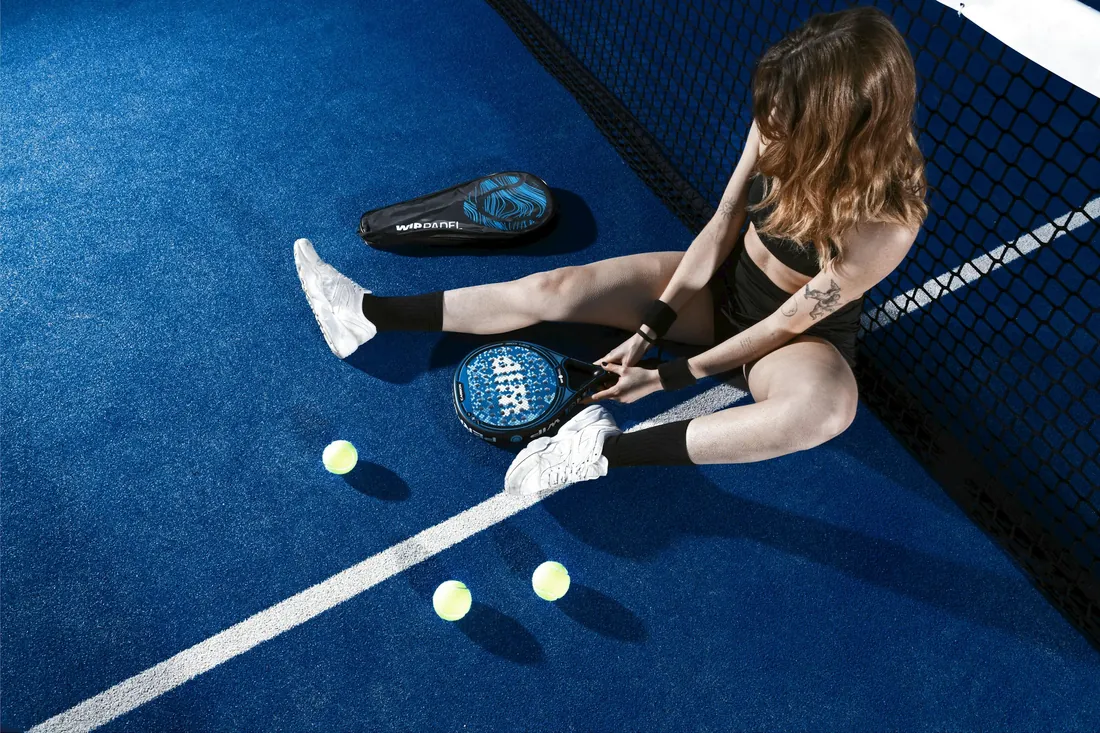 Joueuse assise pres du filet avec sa raquette de padel et trois balles