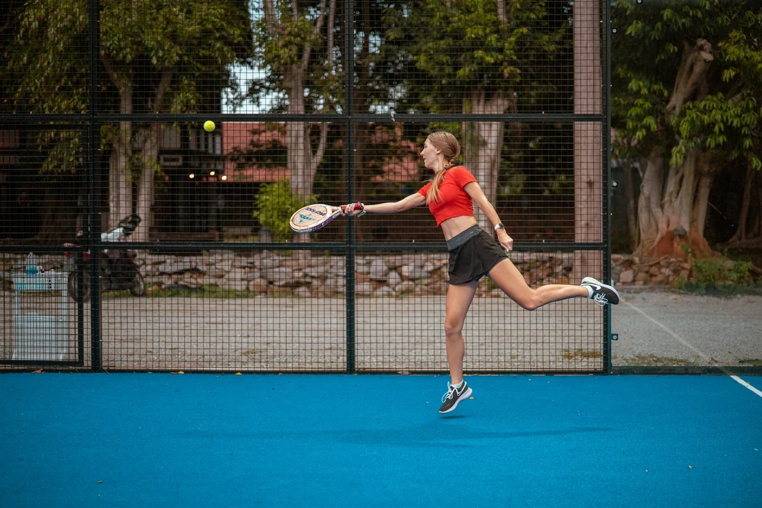 Joueuse de padel en suspension frappant la balle sur une piste bleue entouree de grillage