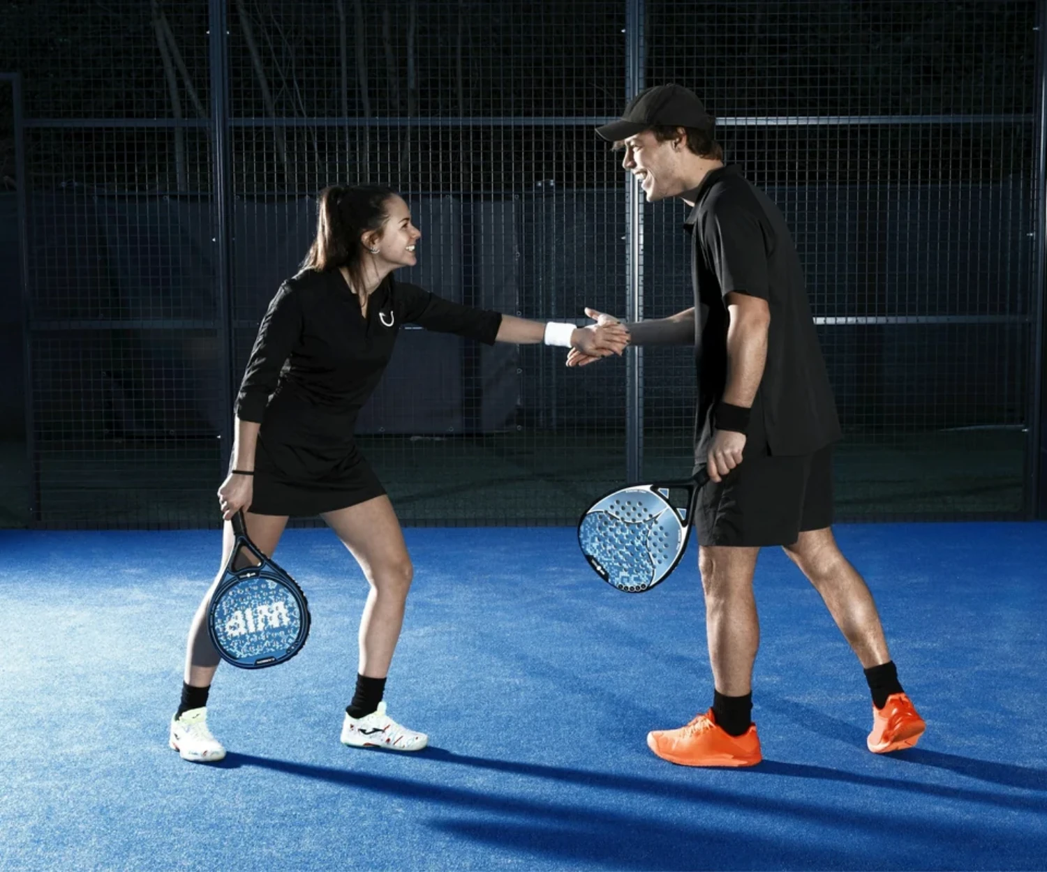 Deux joueurs se serrent la main au filet apres un match sur une piste de padel bleue