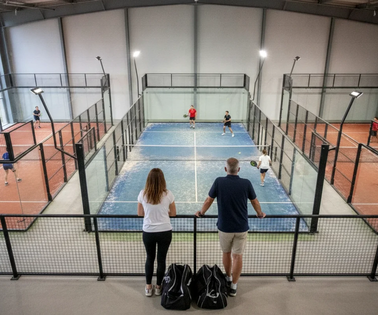 Trois courts de padel couverts à Orléans vus depuis la mezzanine, deux matchs de double en cours