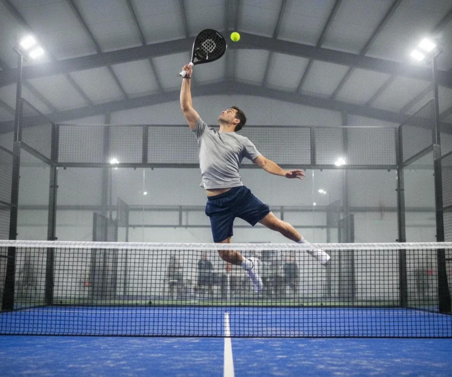 Smash au padel sur un court indoor a sol bleu, illustration du padel a Rouen