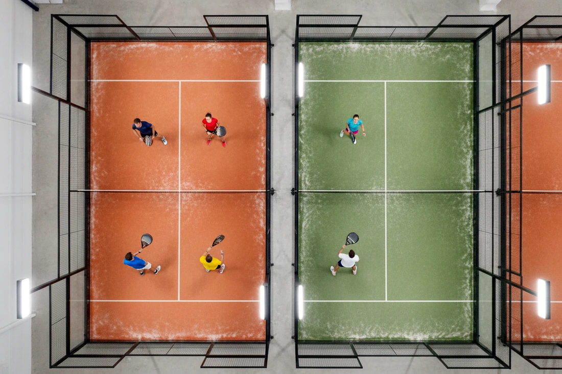 Deux pistes de padel vues du plafond, une occupée à quatre joueurs et l'autre à deux joueurs
