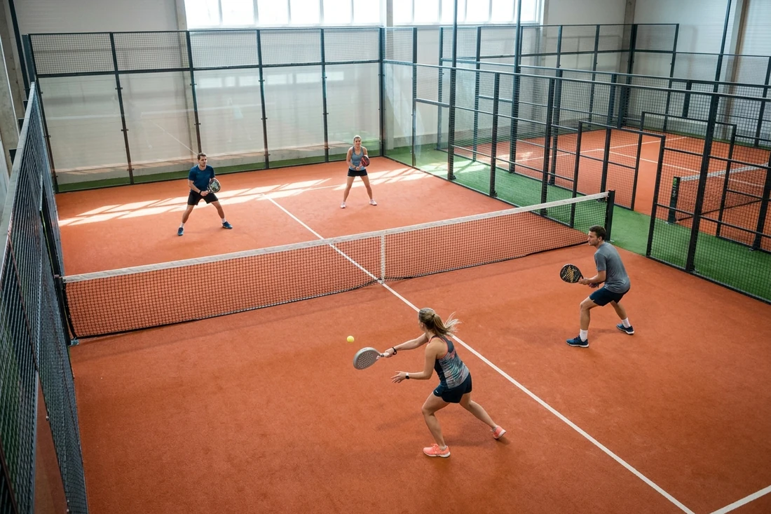 Partie de padel en double vue d'en haut dans un club couvert, une joueuse frappe un coup droit sur un court terre battue