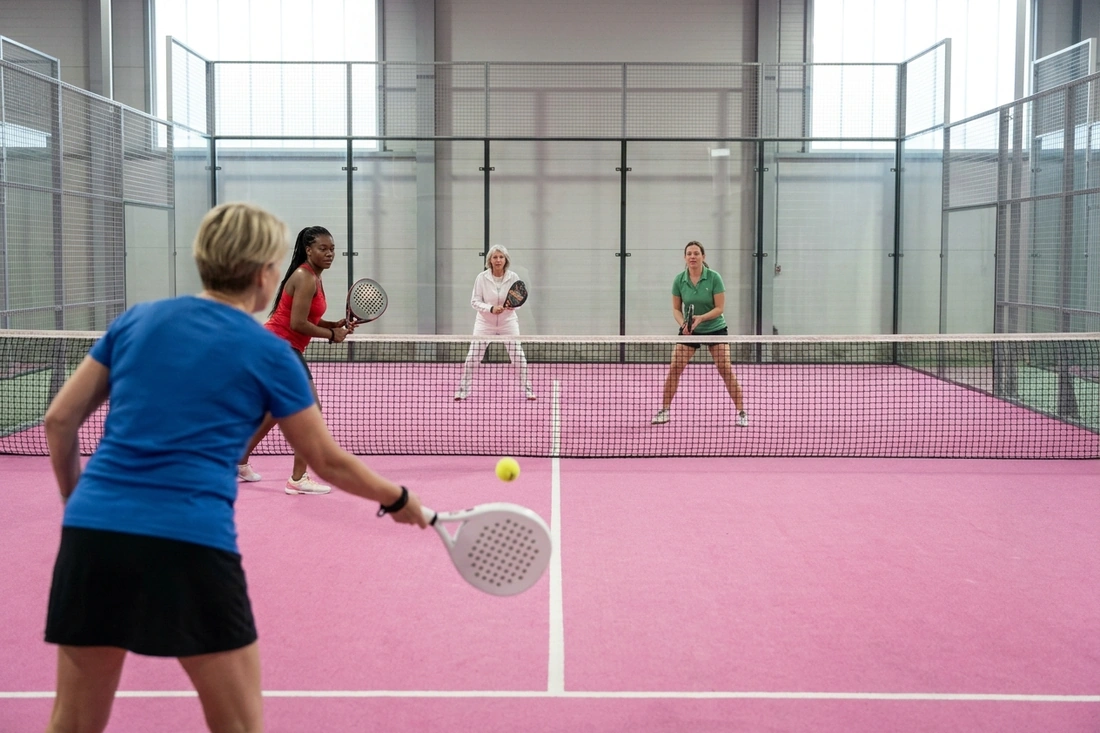 Quatre joueuses de padel en double sur une piste indoor au sol rose, jouer avec une partenaire de son niveau