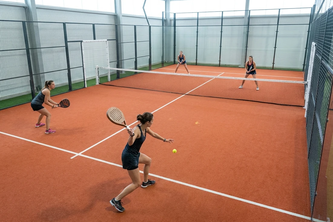 Match de padel en double dames sur une piste indoor au sol orange, une joueuse au service, tournoi dames