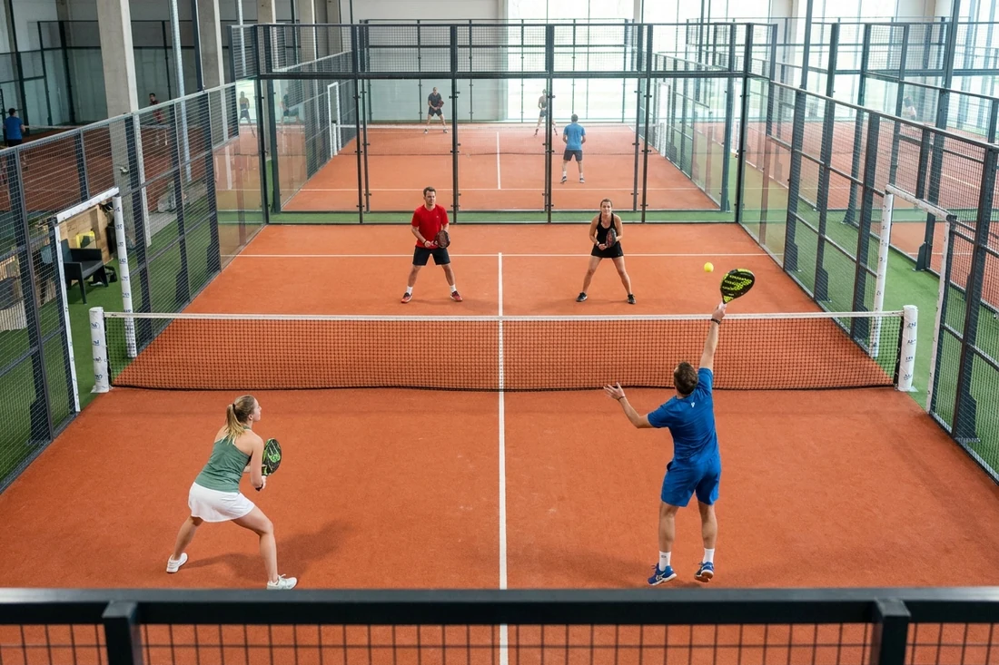 Joueur frappant une bandeja pendant une partie de padel en double sur une piste indoor au sol terre battue