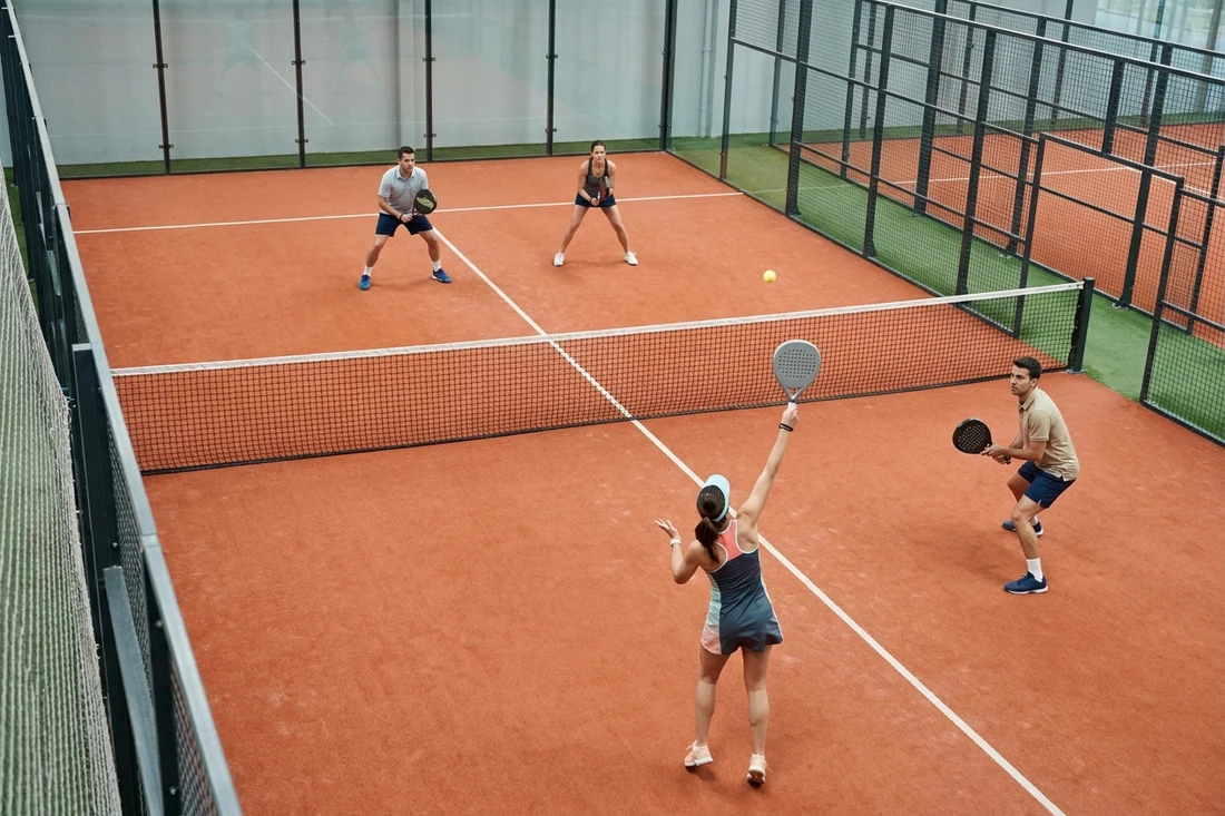 Joueuse de padel frappant une bandeja pendant une partie en double sur une piste indoor au sol orange, tarifs du padel à Nantes