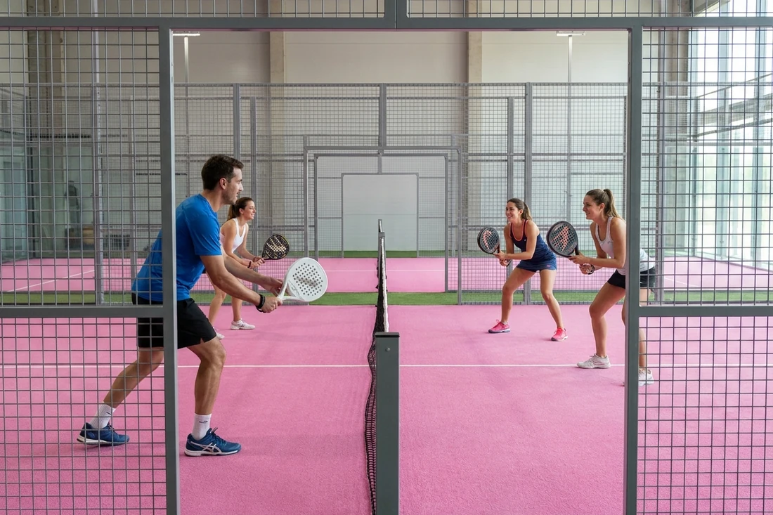Quatre joueurs de padel en position d'attente pendant une partie amicale en double, vue de côté sur un court à sol rose