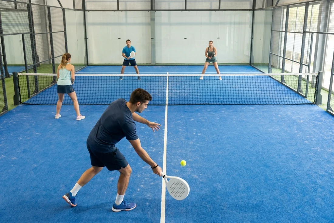 Partie de padel en double vue d'en haut : un joueur sert à la cuillère sur un court indoor bleu